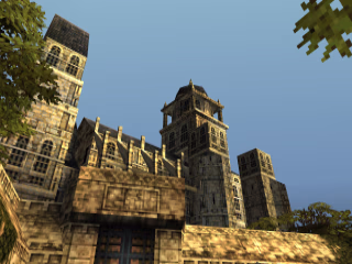 First-person view of a cathedral behind a gate. It has three visible towers and plenty of windows. In the foreground are some leaves from trees behind the camera, and the gate in front of the camera has a closed double door.