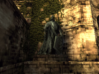 A statue in front of a wall overgrown with ivy. The statue is a man with a sword in his right hand and a shield in his left. He's holding the sword by its pommel and facing it down as if he's leaning on it. He's holding the shield in a similar manner by its side.